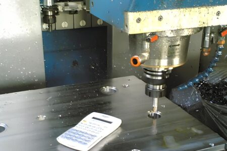 Lavorazione meccanica di precisione su un blocco idraulico in acciaio con centro di lavoro CNC e calcolatrice tecnica per il controllo delle quote.